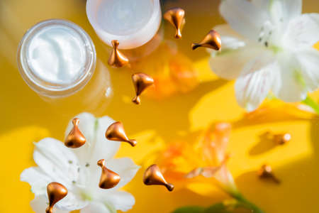 flatlay, composition with cream, flowers on yellow background.Concept of natural beauty,vitamin cosmetic product, skin care. orange small capsules with vitamins for radiance and nutrition of the skinの写真素材