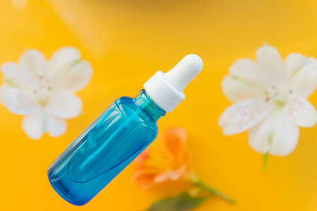 Serum glass bottle with pipette and beautiful flowers on the yellow background. Natural organic spa cosmetic concept. Top view.Beauty face serum with hyaluronic acid and collagen.rejuvenationの写真素材