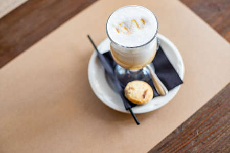 glass of Latte Macchiato with spoon, straw and plate with cookies on a wooden table.Delicious sweet breakfast. Coffee latte macchiato.Coffee in a glassの写真素材