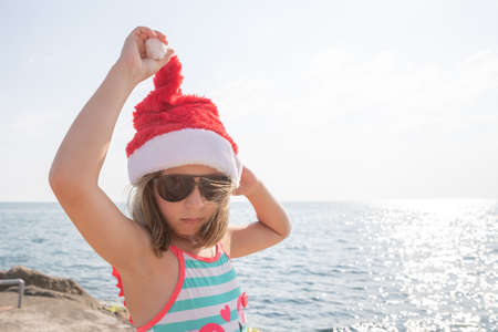 Cute girl celebrating New Year and Christmas on the beach in a hat of Santa Claus. winter holidays in tropical countries.Christmas at tropical resort, vacations travel tourism people conceptの写真素材