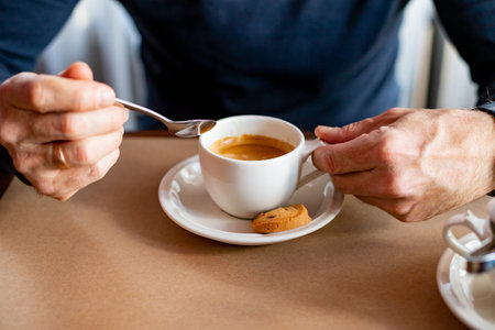 Hand puts a sugar cube in the coffee cup.A mans hand uses a cutlery to take a lump of sugar to add...