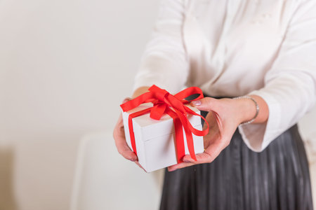 Female hands holding small gift with ribbon.Girl in white shirt holding a white gift box with a red...