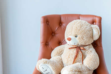 the teddy bear sitting on a brown leather chair.cure3 beige teddy bear sitting alone on armchair in living room. An unexpected surprise gift for a child or girl.の写真素材