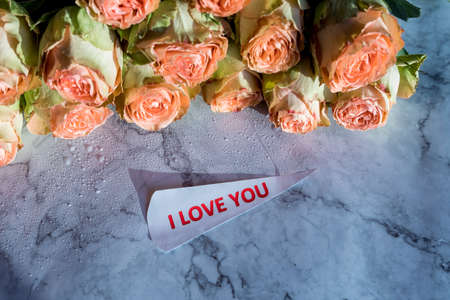 i love you text ,greeting card paper note. Delicate orange roses on marble background. Minimal trendy composition. Romantic pastel rose flowers.Valentines day and love concept.の写真素材