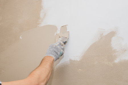 Man plastering wall with putty-knife, preparation for painting.Hands of worker with wall plastering tools renovating house. Plasterer renovating walls and corners with spatula.Copy spaceの写真素材