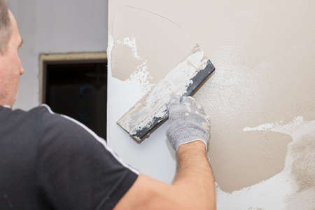Man plastering wall with putty-knife, preparation for painting.Hands of worker with wall plastering tools renovating house. Plasterer renovating walls and corners with spatula.Copy spaceの写真素材