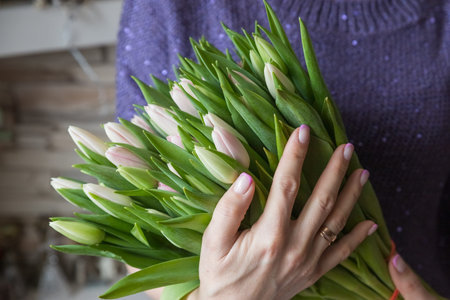 Woman holding bouquet of pink tulips against beige background, big and beautiful bunch of fresh red tulips, cropped photo, bouquet close up.Floral spring background.の写真素材