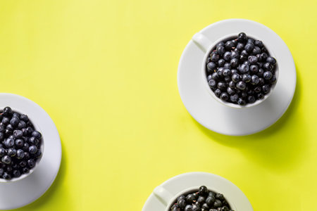 Fresh raw organic farm blueberry in white cup on yellow kitchen background, copy space.Summer seasonal natural vitamines and antioxidants. Healthy diet and nutrition concept.flat layの写真素材