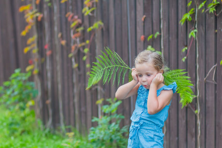 child girl with blond hair is dancing in the park. happy childhood. girl kid whirls in a blue dress near fence in the summer.Positive emotions and happiness concept.Blue Eyed Girl Playing Outsideの写真素材