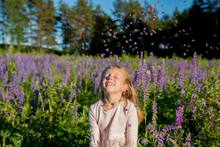 portrait of cute seven year old kid girl with bloom flowers lupines in field of purple flowers. Child throws flowers. nature concept. Provence. Childhood. Summer vacation holidaysの写真素材