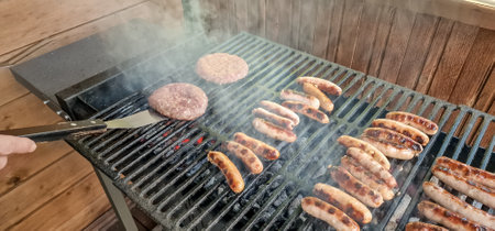 Fresh sausage and hot dogs grilling outdoors on barbecue grill.From above anonymous cook putting grilled sausagesの写真素材
