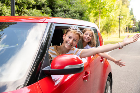 Cheerful little daughter sitting on back seat of car looking at mother while travelling. enjoying road trip. Traveling in car.Exploring nature, travel, family vacation. Mother and child.の写真素材
