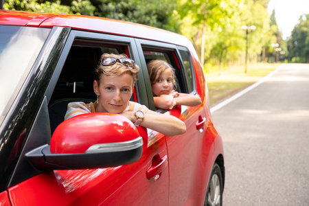 Cheerful little daughter sitting on back seat of car looking at mother while travelling. enjoying road trip. Traveling in car.Exploring nature, travel, family vacation. Mother and child.の写真素材