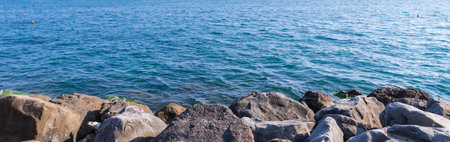 Tranquility rocky beach with big black stones, blue sea and sky as background, tranquil and looks beautiful.Big stone beach in front of sea with skyの写真素材
