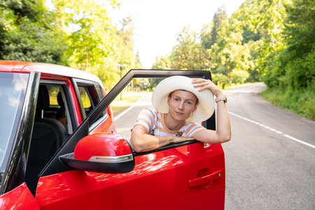 enjoying purchase in dealership, rent a car, travel concept.positive cheerful girl funky driver ,enjoy hits music.Cheerful young female is near shiny red carの写真素材