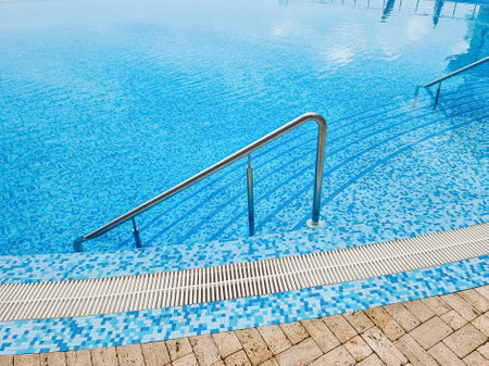 Beautiful pool with a Metal Handrails Descent and blue water at sunset. Swimming and summer rest concept.pool with a metal handrail. Safety for water sportsの写真素材