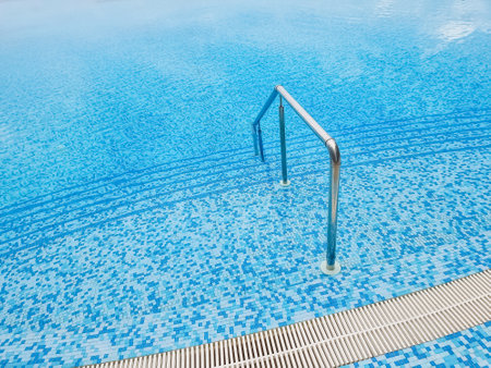 Beautiful pool with a Metal Handrails Descent and blue water at sunset. Swimming and summer rest concept.pool with a metal handrail. Safety for water sportsの写真素材