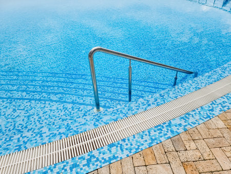 Beautiful pool with a Metal Handrails Descent and blue water at sunset. Swimming and summer rest concept.pool with a metal handrail. Safety for water sportsの写真素材