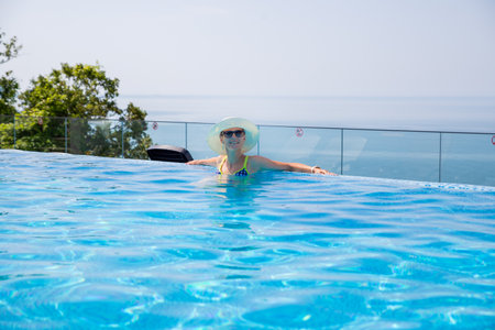 Summer travel vacation concept, Happy traveler asian woman with hat and bikini relax in luxury infinity pool hotel resort at day.beautiful woman with white hat enjoys her vacation in the poolの写真素材