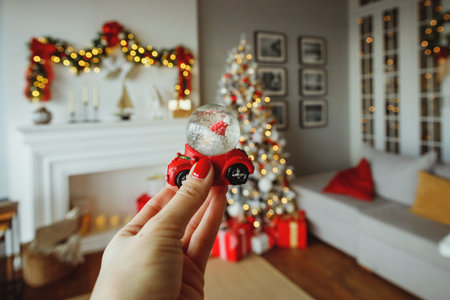 woman hand with snow ball, santa in car. Stylish Christmas interior with an elegant sofa and fireplace. Presents and wrapped gifts under the Christmas tree with light and bauble in sunny living room.の写真素材