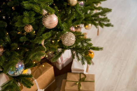 Big beautiful christmas tree decorated with beautiful shiny baubles and many different presents on wooden floor. White wall background with copy space.の写真素材