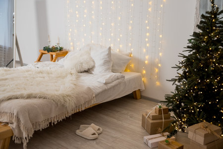 Christmas decorated bedroom interior with comfortable bed, Christmas fir tree and gift boxes on floor, copy space. Cozy home moment. Happy New Year. christmas garland lights at homeの写真素材