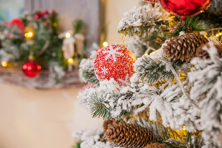 Christmas tree branches on blurred background with red balls and golden decor, berries, garland, cone. Christmas snowy fir tree branches, pine cone. Home decoration, winter holidaysの写真素材