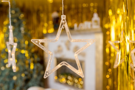 Christmas gold garland on blurred festive background. Happy New Years card.Christmas season, glass lanterns, star hanging in living room as decoration.の写真素材