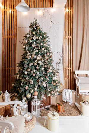 Cozy eco-style living room decorated for Christmas. chair with pillows and blankets near a large Christmas tree decorated with bright garlands and minimalist white, beige toys in a bright interiorの写真素材