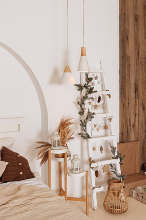cozy New Years decor of the room lit by the magic garland lights. Festive atmosphere before holidays. Scandinavian style. Loft interior with bed with white and grey cushions and wooden shelvesの写真素材