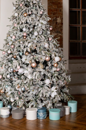 Artificial Christmas tree in a bright interior with silver, pink, bronze balls and snow on the branches. The concept of New year and Christmas. Luxury Christmas tree with glowing garland.の写真素材