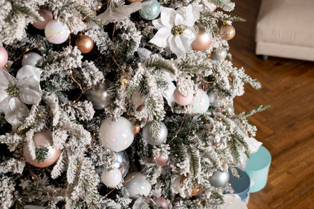 big Christmas tree in a bright interior with silver, pink, bronze balls and snow on the branches. Present boxes under tree. Happy New year and Christmas. Luxury Christmas tree with glowing garland.の写真素材