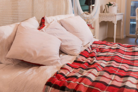 Comfortable double bed with white pillows, red bedding and blanket in cozy bedroom. Stylish interior...