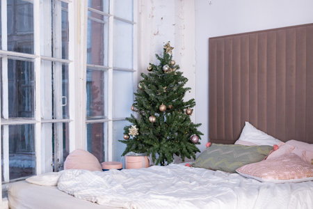 Light Christmas bedroom with Christmas tree. Bed with beige i white pillows, cushions and blanket near Christmas treeの写真素材