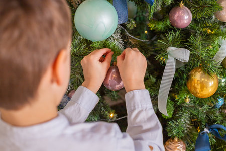 Child decorates Christmas tree. The boy is holding a Christmas toy.Happy New Year. Family decorating a Christmas tree with balls. The morning before christmas at home. Decorated interiorの写真素材