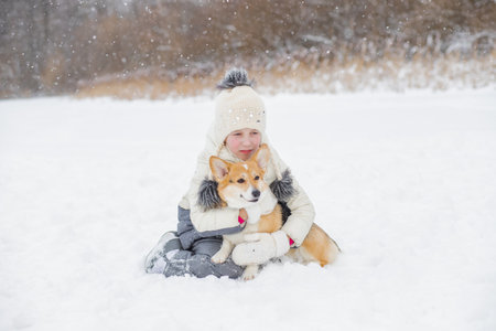 happy child having fun in snowy winter park with Corgi baby dog.Walking the dog in the park in winter. girl plays with corgi. copy spaceの写真素材