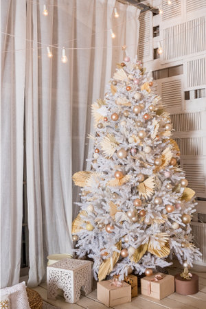 snow-covered Christmas tree with white, golden, bronze decorations and lights. Cozy Christmas tree and gift boxes in interior.Brightly lit christmas tree with lots of gifts.New year greeting card.の写真素材