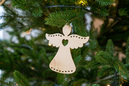 Handmade Christmas angel hangs on a branch of a Christmas tree with balls and wooden toys. Christmas zero-waste ornaments. wooden eco toys. New year decor.の写真素材