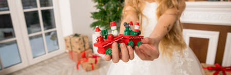 Hands of a child holding a gift, A wooden train toy is carrying New Years gifts. Cozy home New Year atmosphere.wooden vintage train. web bannerの写真素材