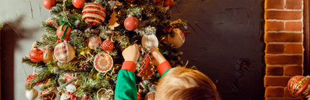 Close up of little Caucasian girls hands putting ornaments on Christmas tree styled in red and...