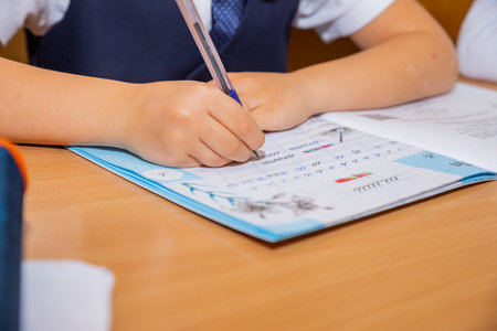 Close-up cropped shot of unrecognizable pupil boy studying at home writing in exercise book doing homework, learning sitting at table. schoolboy doing homework, Writing hand of school child on lesson.の写真素材