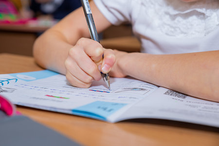 Close-up cropped shot of unrecognizable pupil boy studying at home writing in exercise book doing homework, learning sitting at table. schoolboy doing homework, Writing hand of school child on lesson.の写真素材