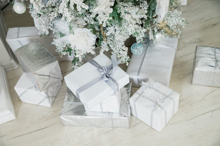 Beautiful Christmas gift boxes on floor near fir tree in room. Traditional christmas pine tree with...