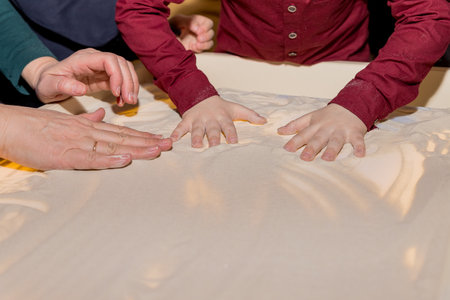 Little girl paints on a white table with sand, salt, close up. art lesson. DIY Play and Learn Activities for Kids. children are playing with sand on glass table. Imagination lessonsの写真素材