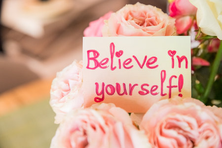 A yellow greeting card with words Believe in Yourself laying on a big bouquet of colorful roses.Valentines day concept. Gratitude gratefulness, believe concept.Flowers deliveryの写真素材