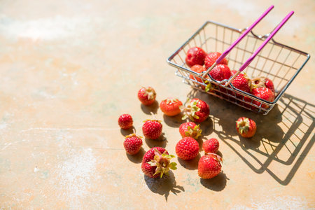 Fresh berries, shopping trolley in which red ripe strawberries, and some strawberry lying next to shopping cart , on yellow background.healthy and tasty low carb berry conceptの写真素材