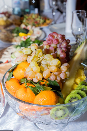 Banquet table served with fruits in the vase. Various fruits on the festive table. Grapes and kiwi.Beautiful giving of fruit at restaurant for a holidayの写真素材