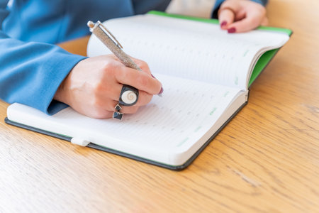 Female hand take notebook form table. Woman works at home. Psychotherapist takes notes about patients condition on paper during sessionの写真素材