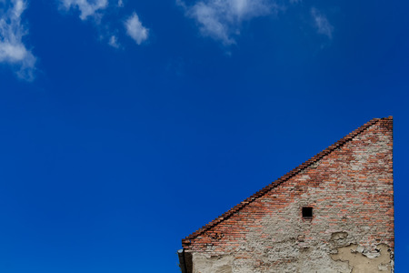 Lonely house. Wall made of bricks creates a triangle. Bright blue sky with several small clouds.の写真素材