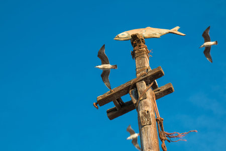 Column with a fish, statue in a port in Essaouira, Morocco. Seagulls flying around. Bright blue sky.の写真素材